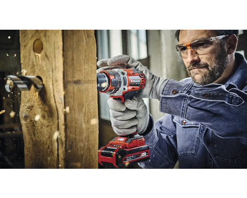 Een man boort met een accuboormachine een gat in een houten plank.