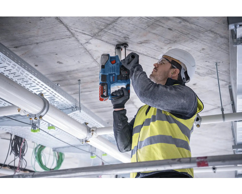 Een man bevestigt met een accuboorhamer een beugel aan een betonnen plafond.