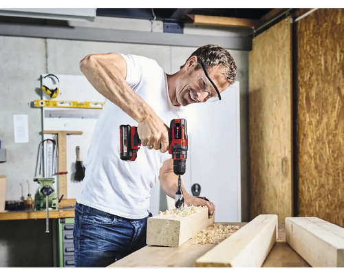 Een man boort met een accuschroefboormachine in een stuk hout in een werkplaats.