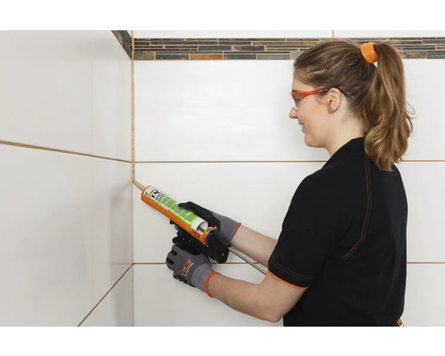 Vrouw dicht voegen tussen tegels af met siliconen.