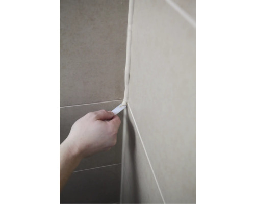 Iemand maakt een voeg glad met een gereedschap.