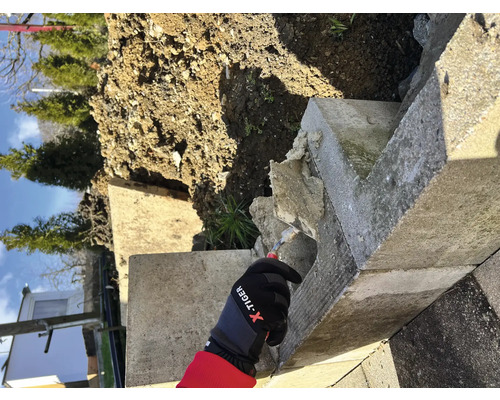 Werknemer met handschoenen tijdens reparatiewerkzaamheden aan een betonnen muur in de tuin.