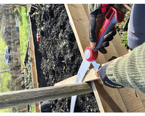 Persoon zaagt een houten plank met een handzaag in de tuin.