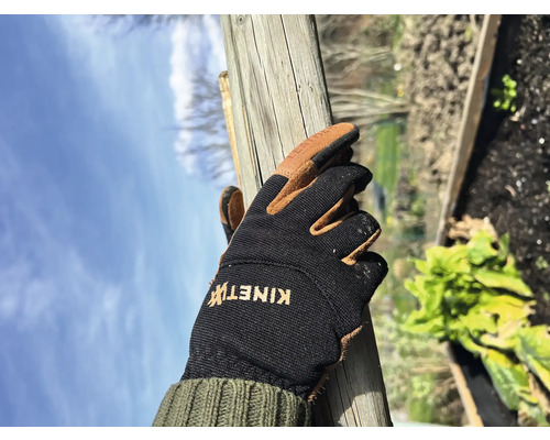 Een hand in een tuinhandschoen houdt een houten paal vast.