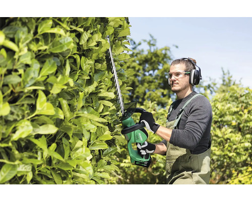 Man snoeit een haag met een heggenschaar. Hij draagt beschermende kleding.