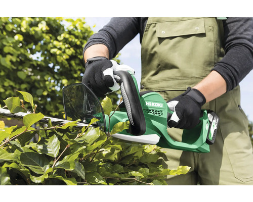 Een persoon snoeit een haag met een accu heggenschaar van het merk Hikoki.