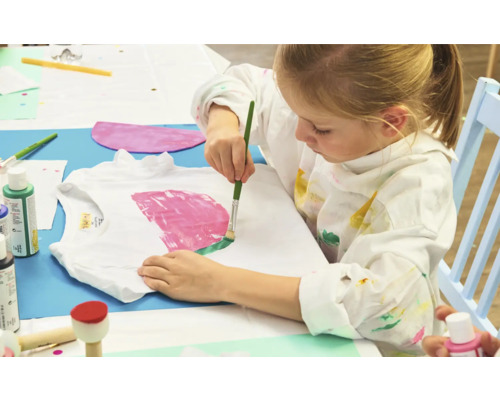 Een kind schildert een T-shirt met een penseel.