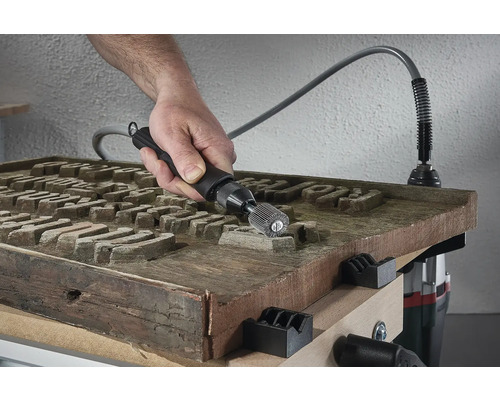 Een persoon gebruikt een multifunctioneel gereedschap met as op een houten oppervlak om het te bewerken.