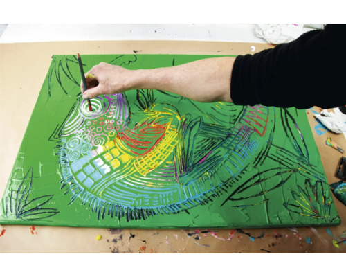 Een persoon schildert met penseel en verf op een canvas. Het canvas toont een abstract ontwerp.
