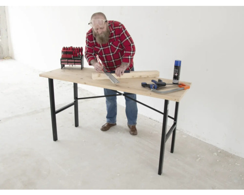 Een man werkt aan een houten tafel met gereedschap zoals schroevendraaiers, een handzaag en een spuitbus.
