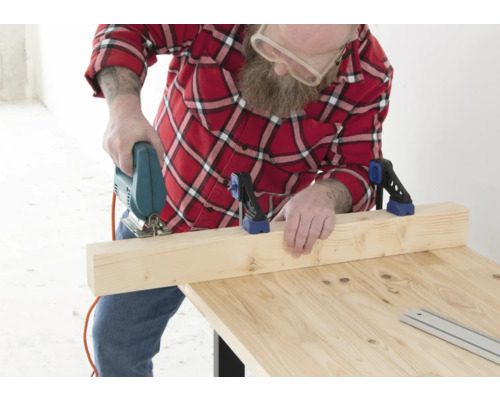Man zaagt houten plank met decoupeerzaag op houten tafel