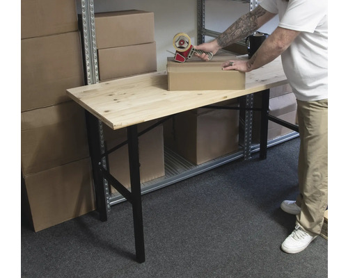 Een persoon verpakt een kartonnen doos met een tapedispenser op een houten tafel in een opslagruimte.