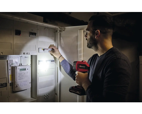 Een man inspecteert een zekeringkast met een Einhell lamp.