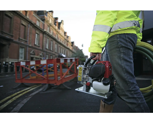 Een bouwvakker draagt een mobiele waterpomp op een bouwplaats.