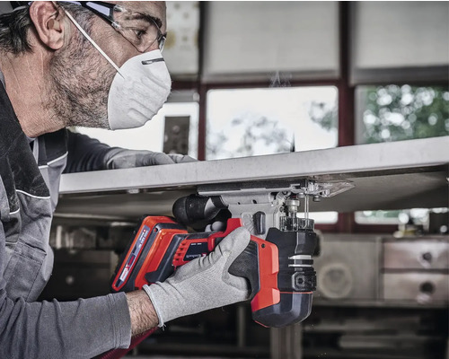 Een man gebruikt een accuslagschroevendraaier voor houtbewerking, veiligheidsbril en gezichtsmasker worden gedragen.