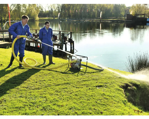 Twee arbeiders bedienen een waterpomp aan de oever van een meer om water te verplaatsen.