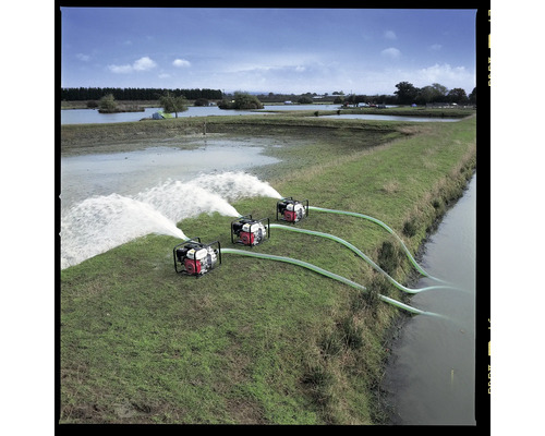 Drie waterpompen in werking op een groene weide naast een waterpartij