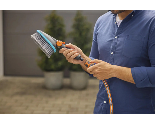 Een persoon houdt een wasborstel met wateraansluiting in zijn hand.