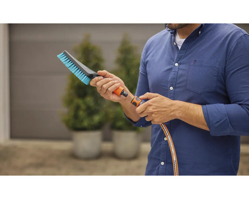 Man verbindt een borstel aan een tuinslang voor schoonmaakwerkzaamheden buitenshuis.