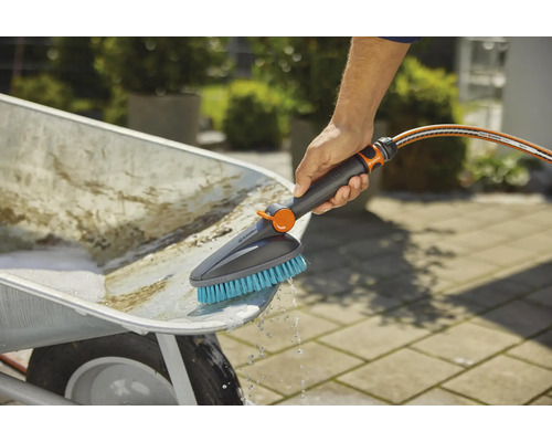 Persoon reinigt een kruiwagen met een borstel en een waterslang