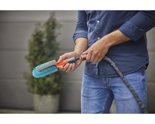 Een persoon houdt een wasborstel met wateraansluiting vast.