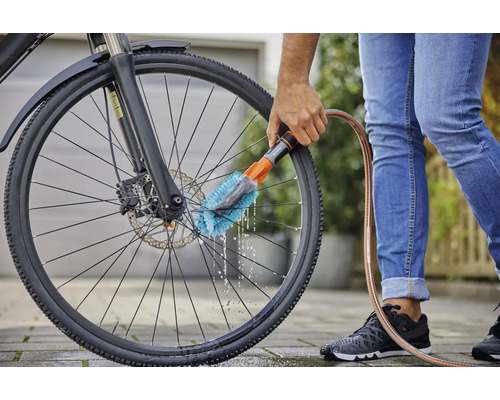Een persoon maakt een fietswiel schoon met een borstel en een waterslang
