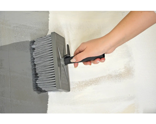 Een hand houdt een blokkwast vast om verf op een muur aan te brengen.