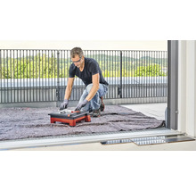 Een man snijdt tegels met een tegelsnijmachine op een balkon.