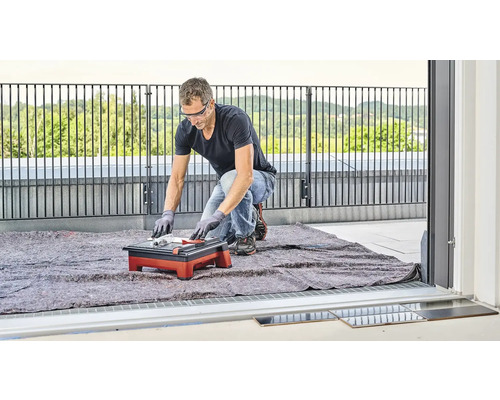 Een man snijdt tegels met een tegelsnijmachine op een balkon.