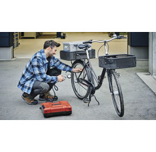 Man pompt fietsband op met een compressor. De fiets heeft manden en een bagagedrager.