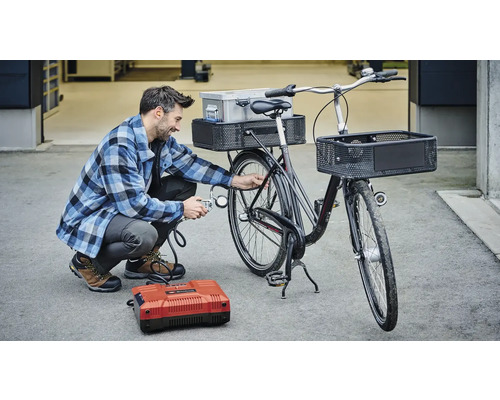 Man pompt fietsband op met een compressor. De fiets heeft manden en een bagagedrager.