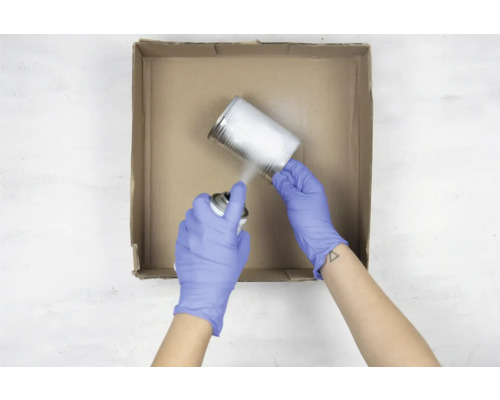 Een persoon met handschoenen spuit verf op een blik in een kartonnen doos.