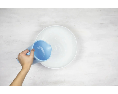 Een persoon giet water uit een kan in een kom.