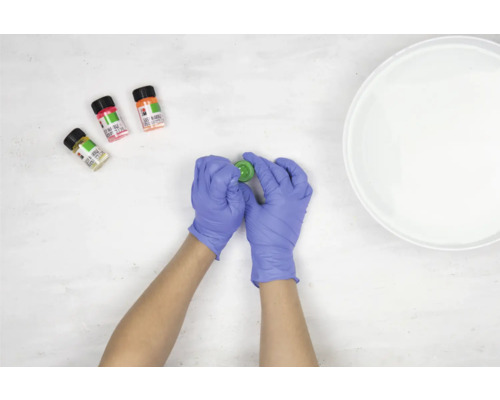 Een persoon met handschoenen opent een marmereffectverf, met drie andere kleuren en een kom water ernaast.