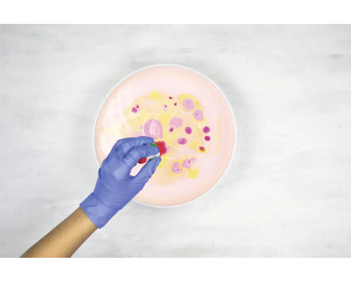 Een persoon met handschoenen voegt verf toe aan een bak om een marmereffect te creëren.