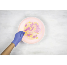 Persoon met handschoenen marmeren kleuren in een kom.