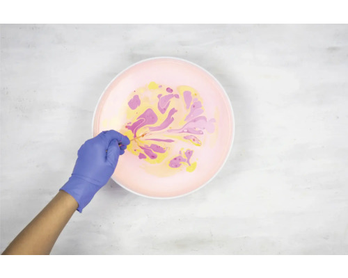 Persoon met handschoenen marmeren kleuren in een kom.