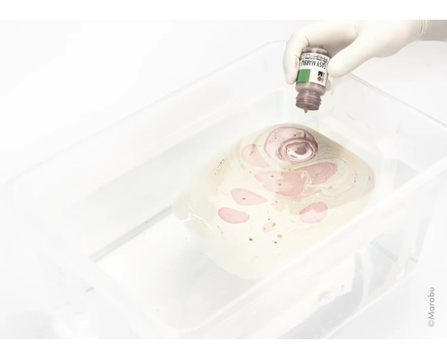 Een gehandschoende hand druppelt marmereffectverf in een waterbad voor marmereffecttechniek.