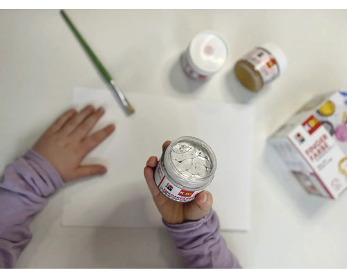 Kind houdt verfpot boven papier, penseel en andere verfpotten liggen klaar