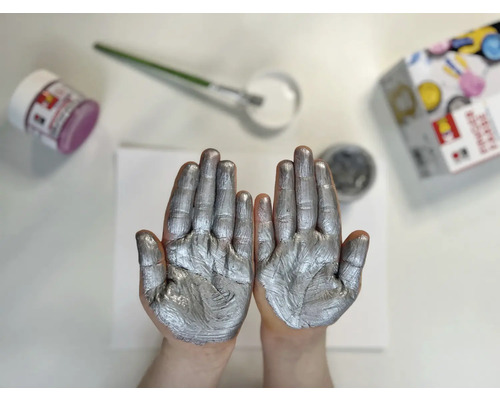 Twee handen met zilververf, verfpotten en penseel op een tafel