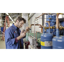 Een man in werkkleding inspecteert een koelaggregaat in een technische ruimte.