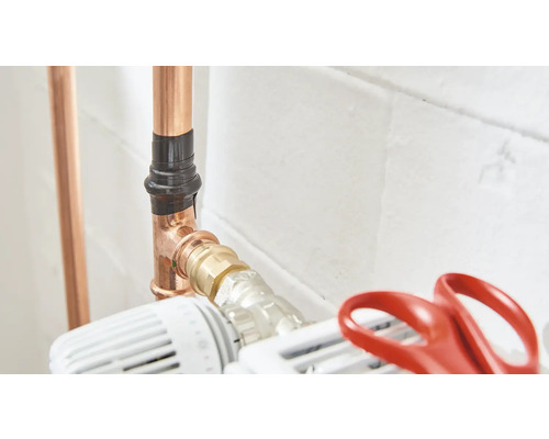 Koperen buizen zijn met zwarte isolatietape en een thermostaatkraan aan de verwarming bevestigd.