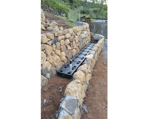 Drainagesysteem installatie langs een stenen muur in de tuin.