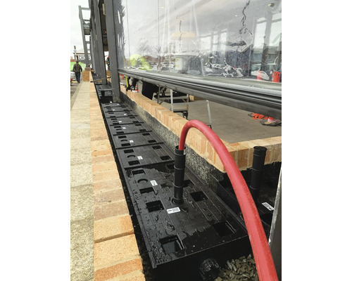 Installatie van een infiltratiesysteem voor regenwaterafvoer met kunststof modules naast een gebouw.