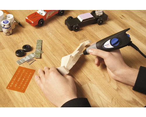 Ambachtelijke scène met Dremel multifunctioneel gereedschap, houten modelauto en accessoires op houten tafel.