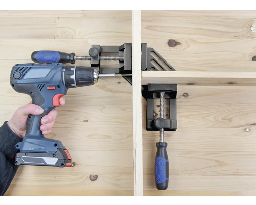 Een persoon schroeft met een accuboormachine een werkstuk vast dat is vastgezet met een hoekklem.