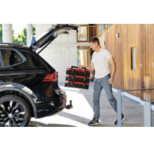 Man laadt rode gereedschapskoffers uit een zwarte auto