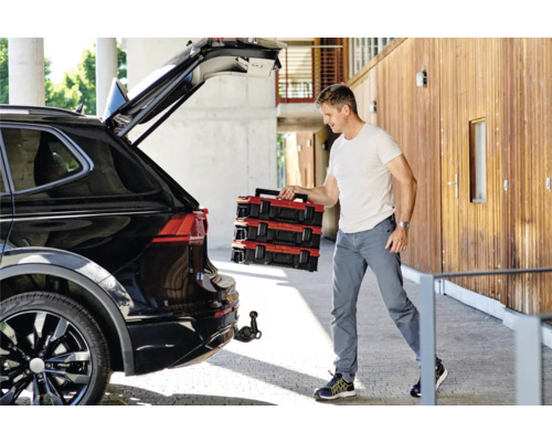 Man laadt rode gereedschapskoffers uit een zwarte auto