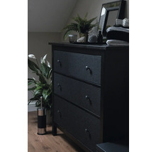Donkere ladekast met drie laden, spiegel, plant en decoratie in een slaapkamer.