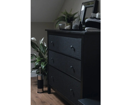 Donkere ladekast met drie laden, spiegel, plant en decoratie in een slaapkamer.